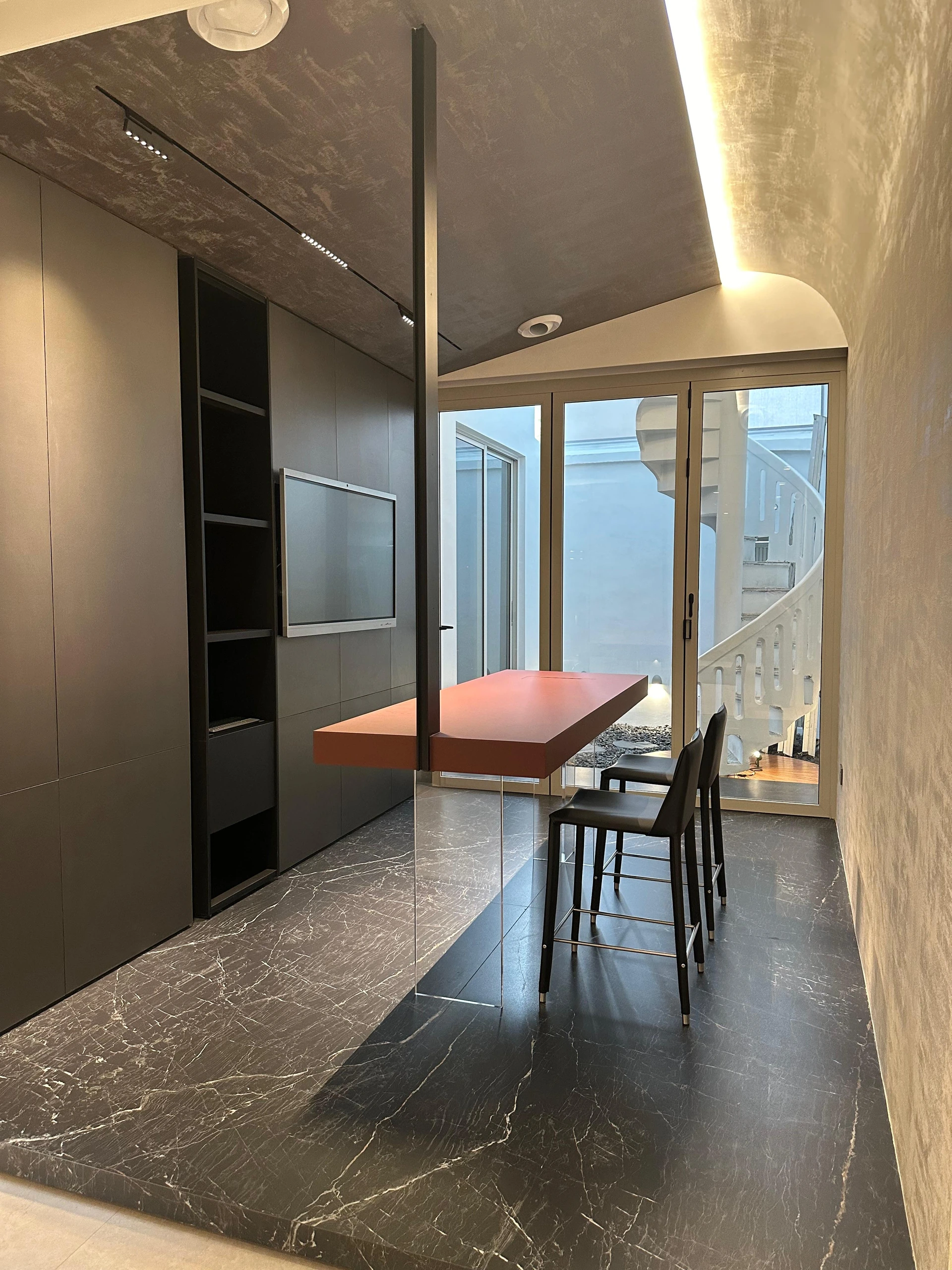 Red dining table in dark stone-lined nook by Edgeline Planners
