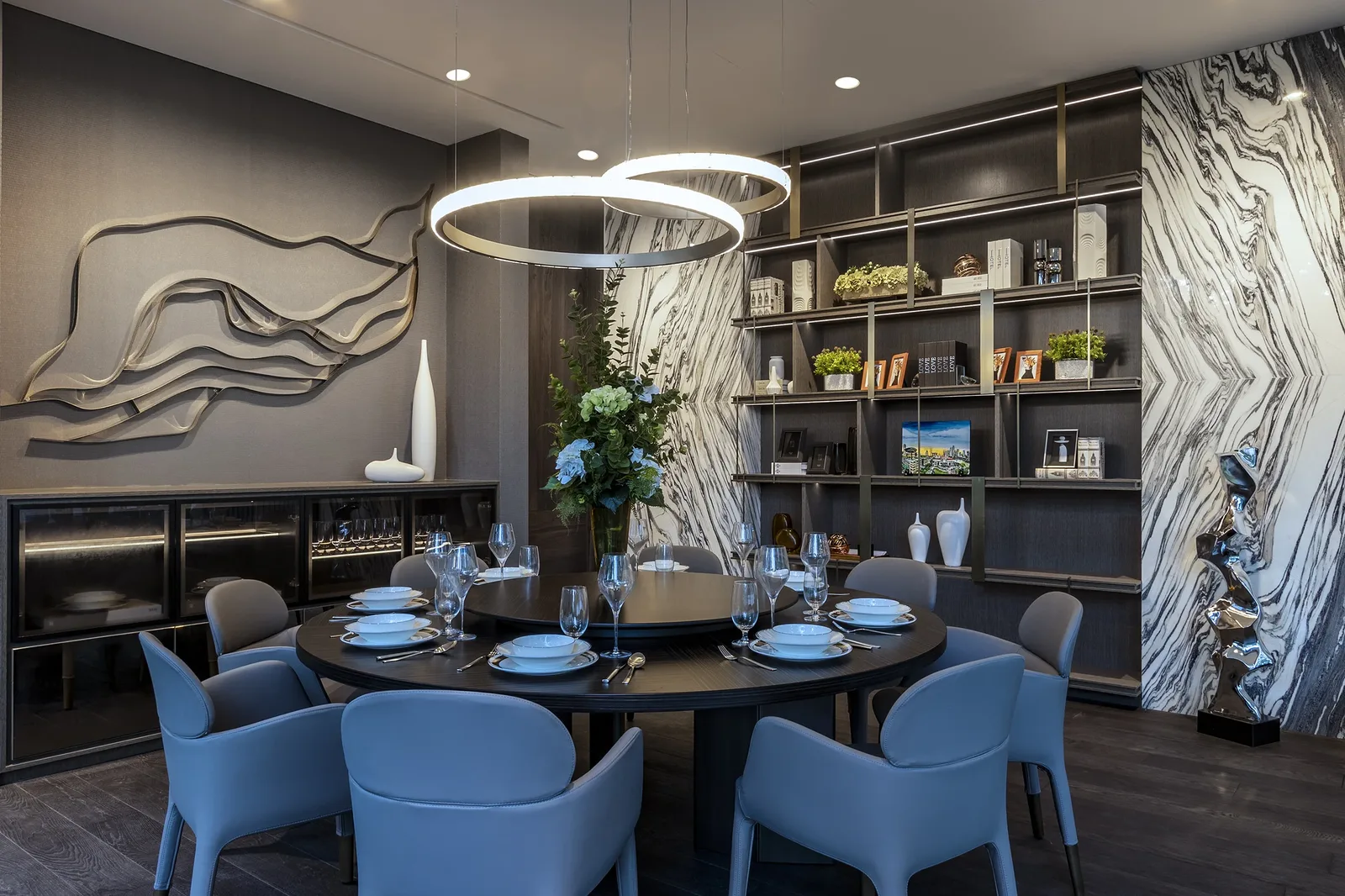 SuMisura &mdash; dining room with ring chandeliers, illuminated display cabinetry and bookmatched marble wall